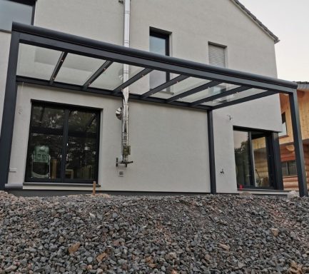 Moderne Hausansicht mit überdachter Terrasse und Kiesfläche im Vordergrund.