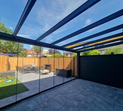 Moderne Überdachung mit Glaswänden und Blick auf den Garten mit Möbeln.