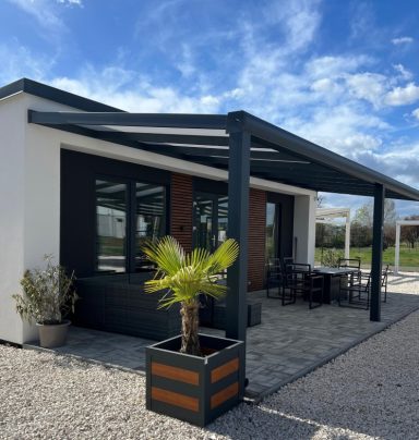 Modernes Haus mit Terrasse, Palmenpflanze und Tischen im Freien unter blauem Himmel.