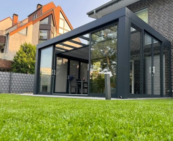 Moderne Glasveranda mit schwarzem Rahmen in einem grünen Garten.